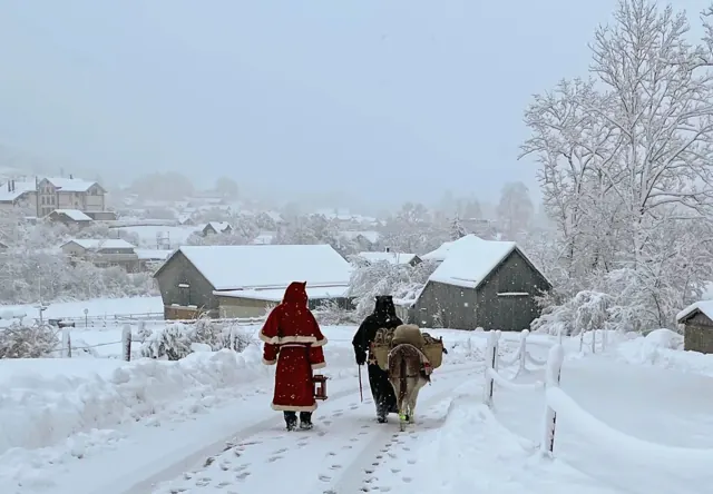 Samichlaus, Schmutzli und Esel gehen auf einer verschneiten Strasse ins Dorf